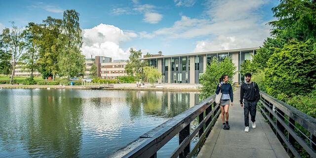 Two students walk across the bridge over the loch, Edinburgh Campus