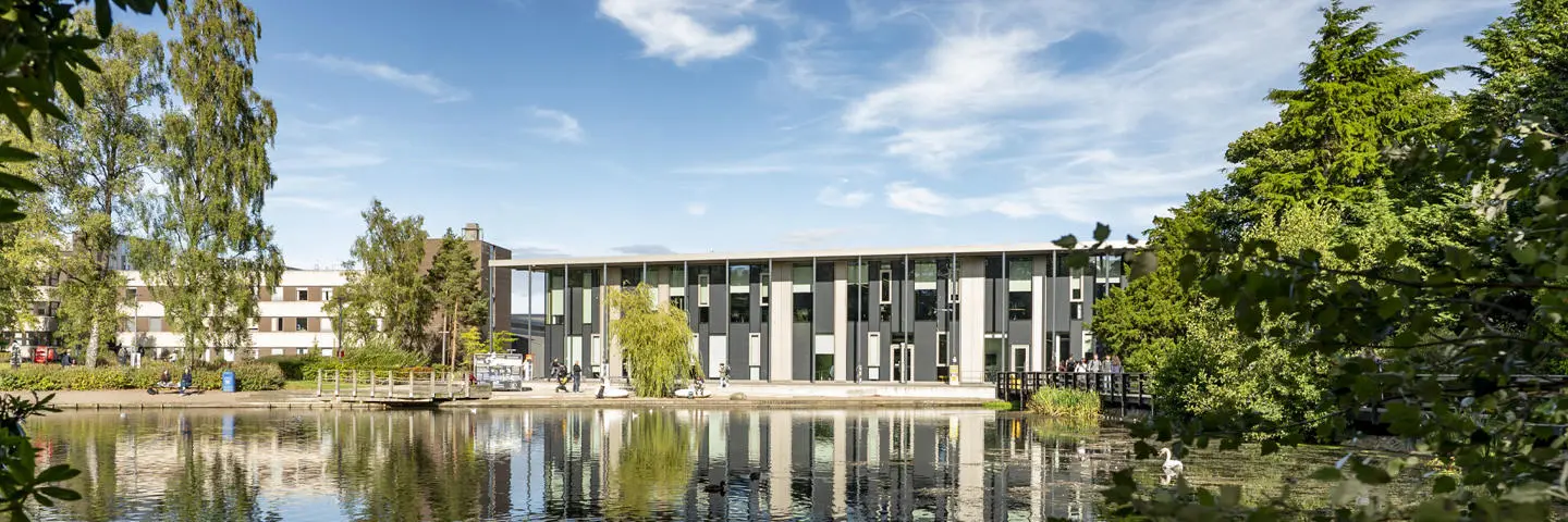 The GRID building stands behind a serene Loch, reflecting its structure in the calm water.