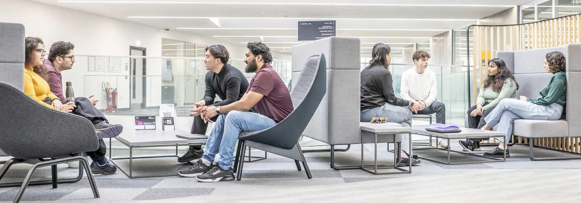 Two groups of seated students in the GRID building break out area.