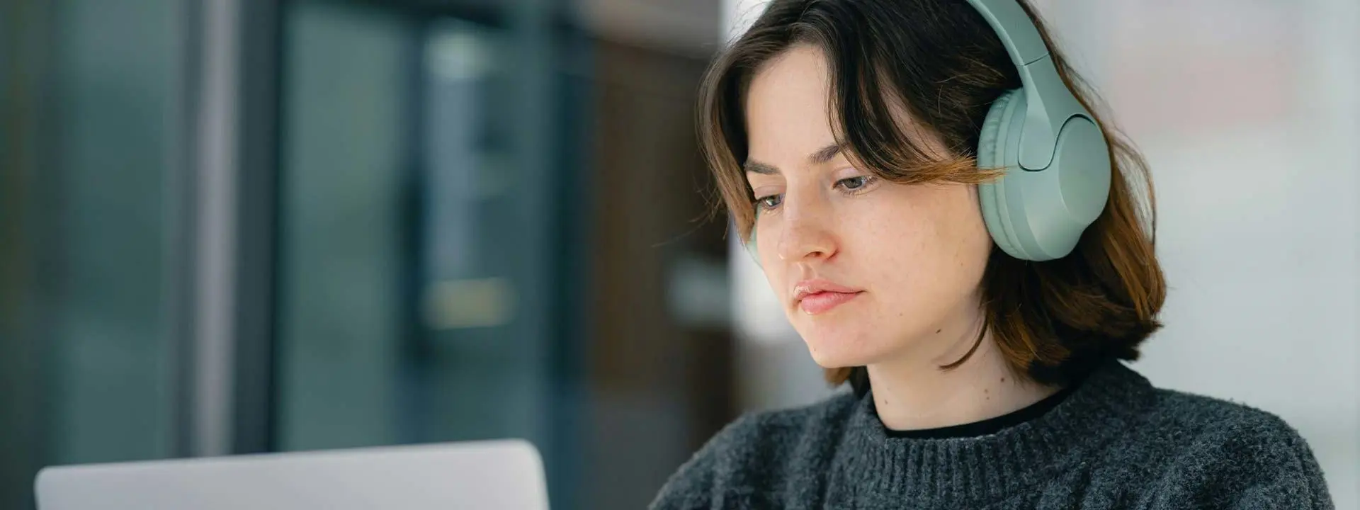 A student with headphones sits at a desk, focused on her laptop while studying.