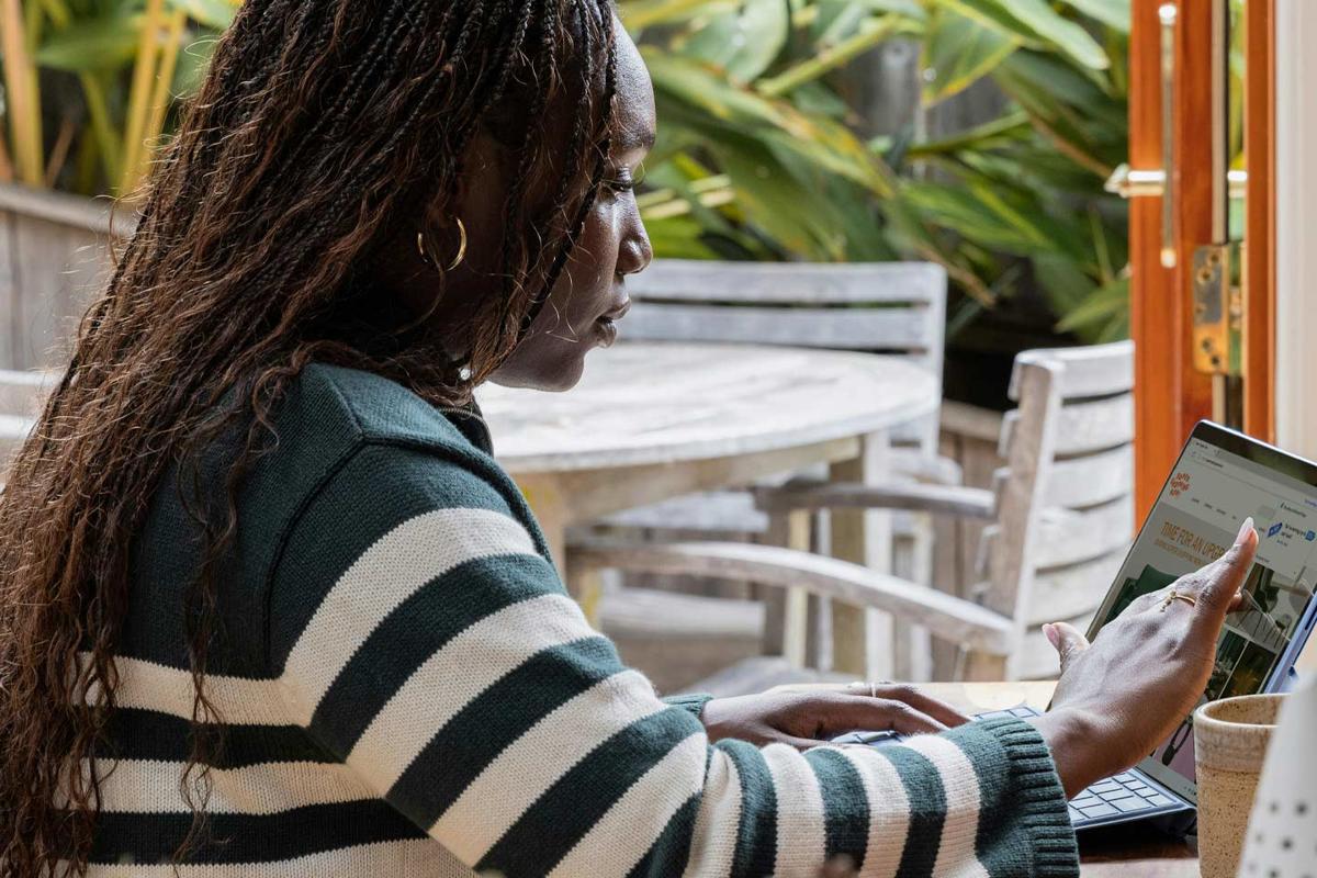 A woman seated at a table, focused on her laptop.