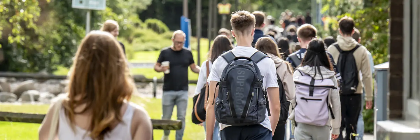 A group of students walking on a path, surrounded by grass and trees.