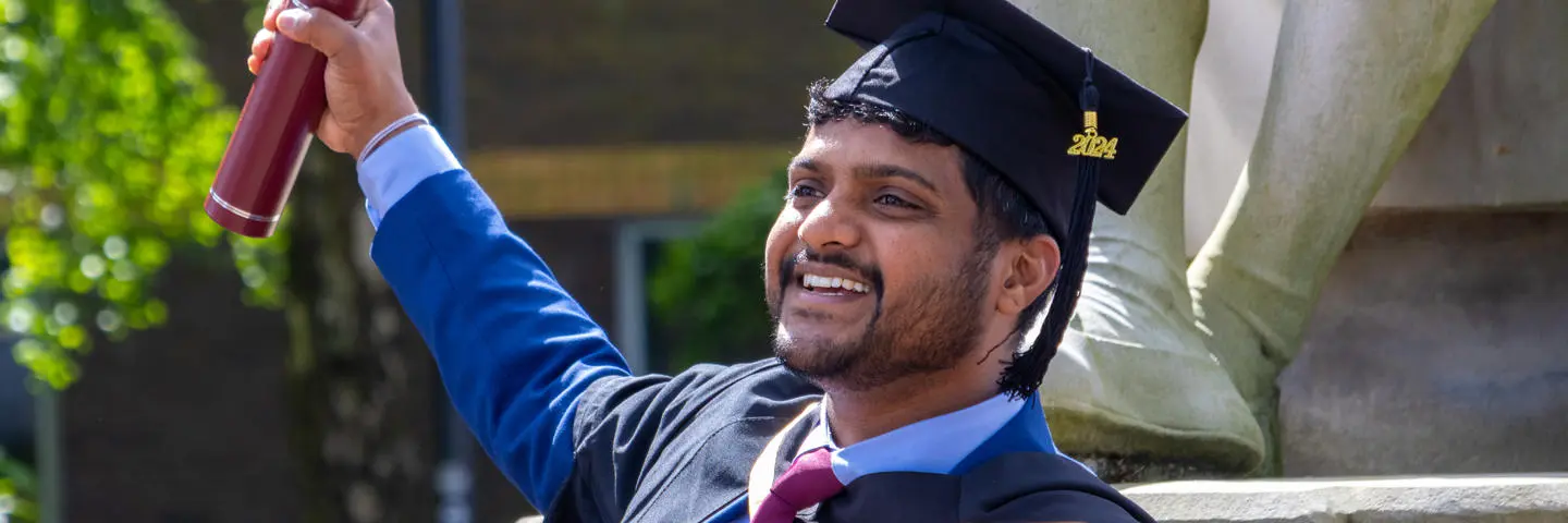 A man holds up a certificate holder on graduation day