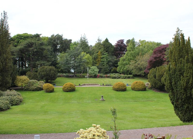 The Lawn viewed from the site of the old Riccarton House Garden lawn with large circular bushes, water fountain and tall trees