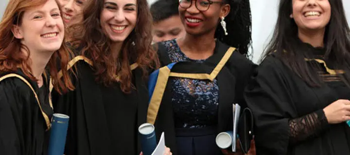 Graduates in gowns holding degrees and smiling