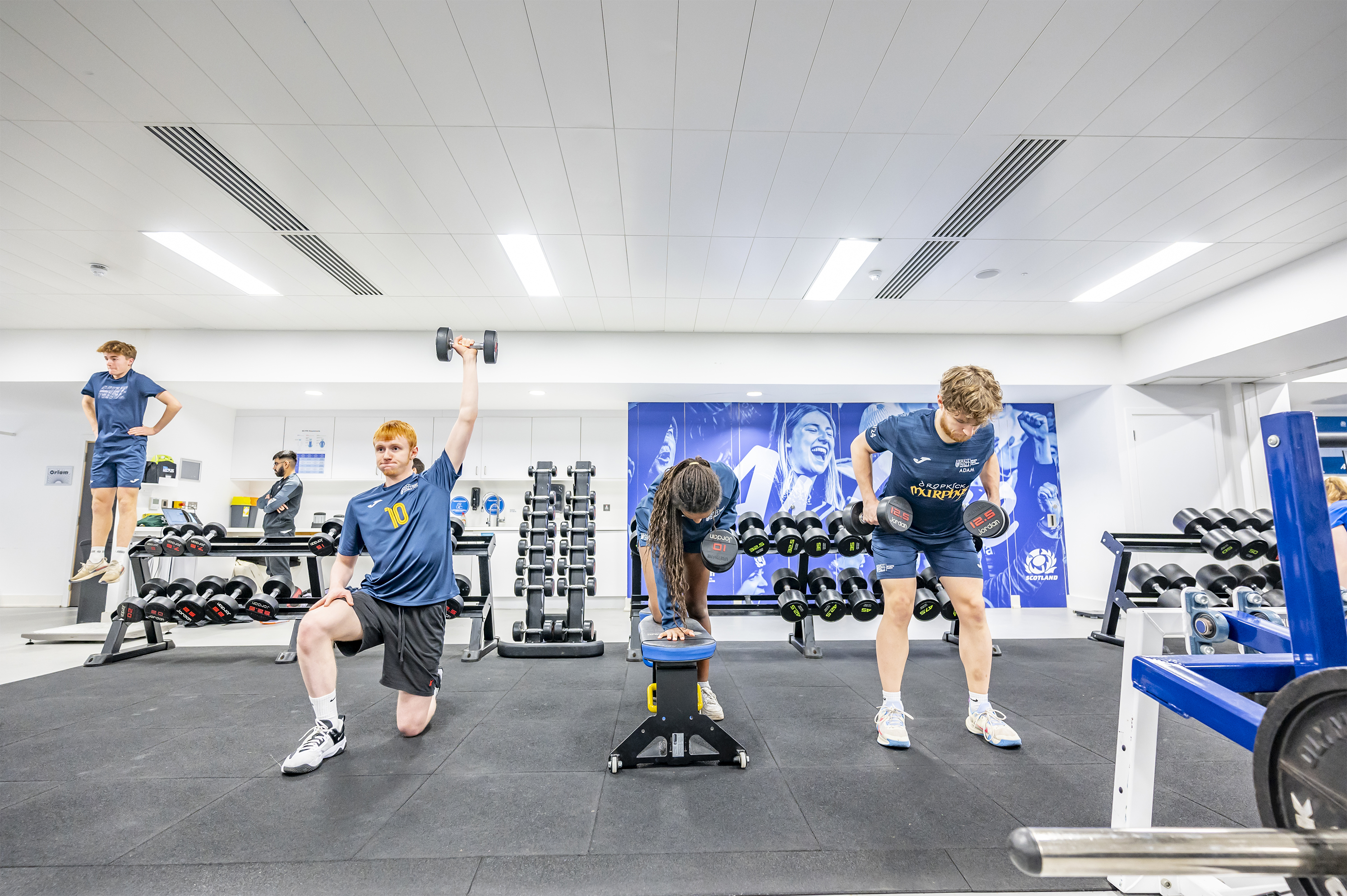 Students exercising together in a gym, using various equipment and engaging in different workouts.