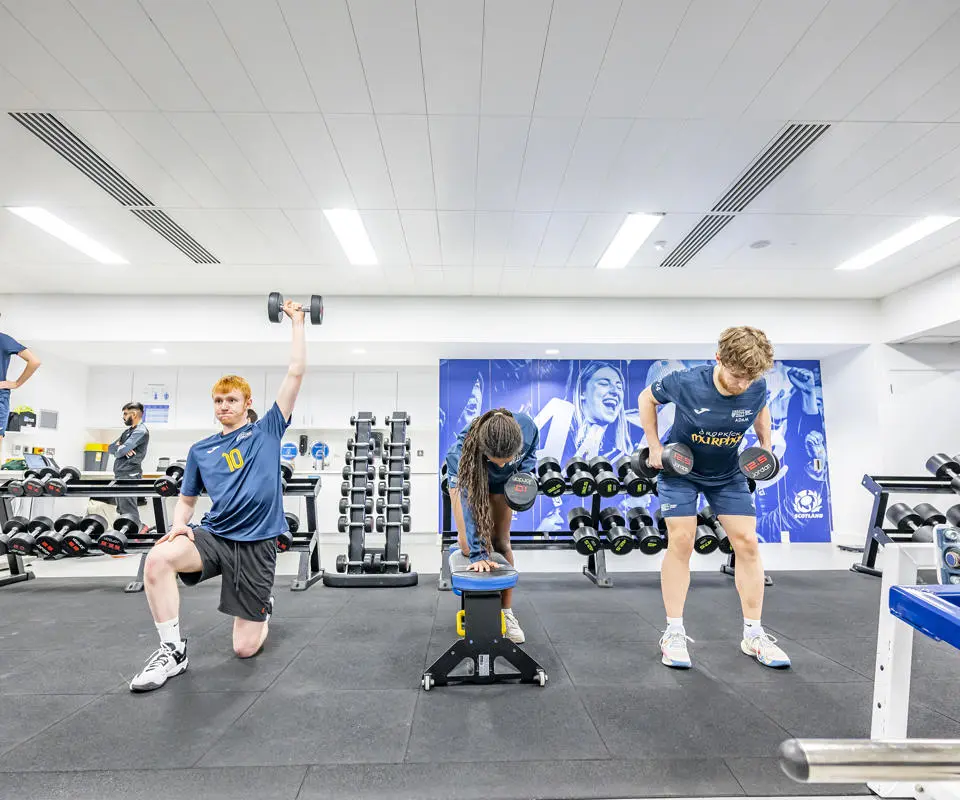 Students exercising together in a gym, using various equipment and engaging in different workouts.