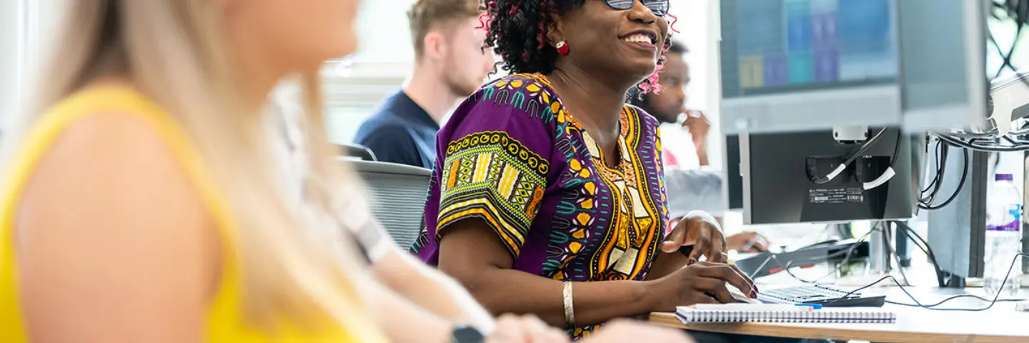 A smiling woman works at a desk and on a computer in an office.
