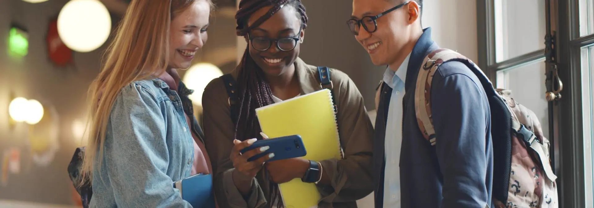 Three students standing in a corridor looking at a phone.