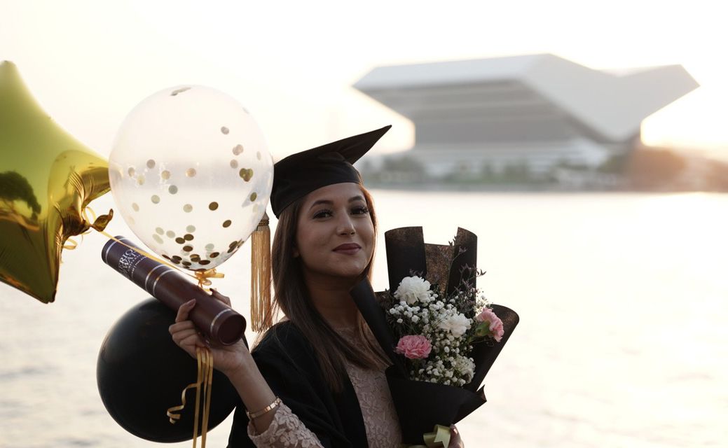 A Dubai graduate holding balloons and flowers. 