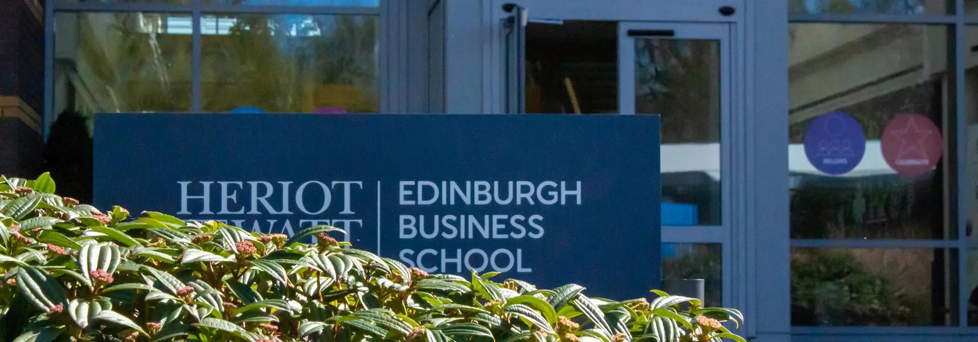 A leafy bush in front of the Heriot-Watt Edinburgh Business School entrance and sign.