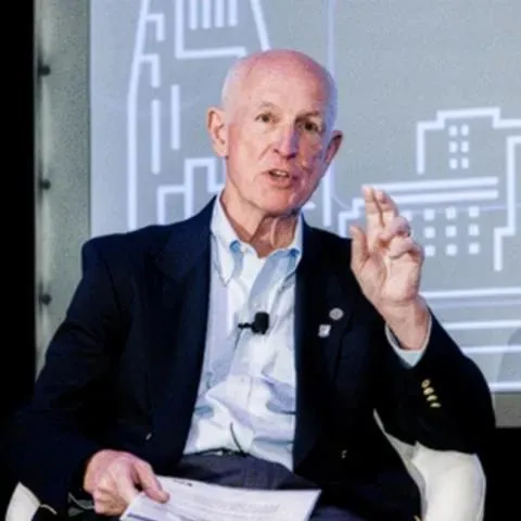 Ian Duncan during a talk, man seated giving a presentation, wearing blue open collared shirt and black jacket