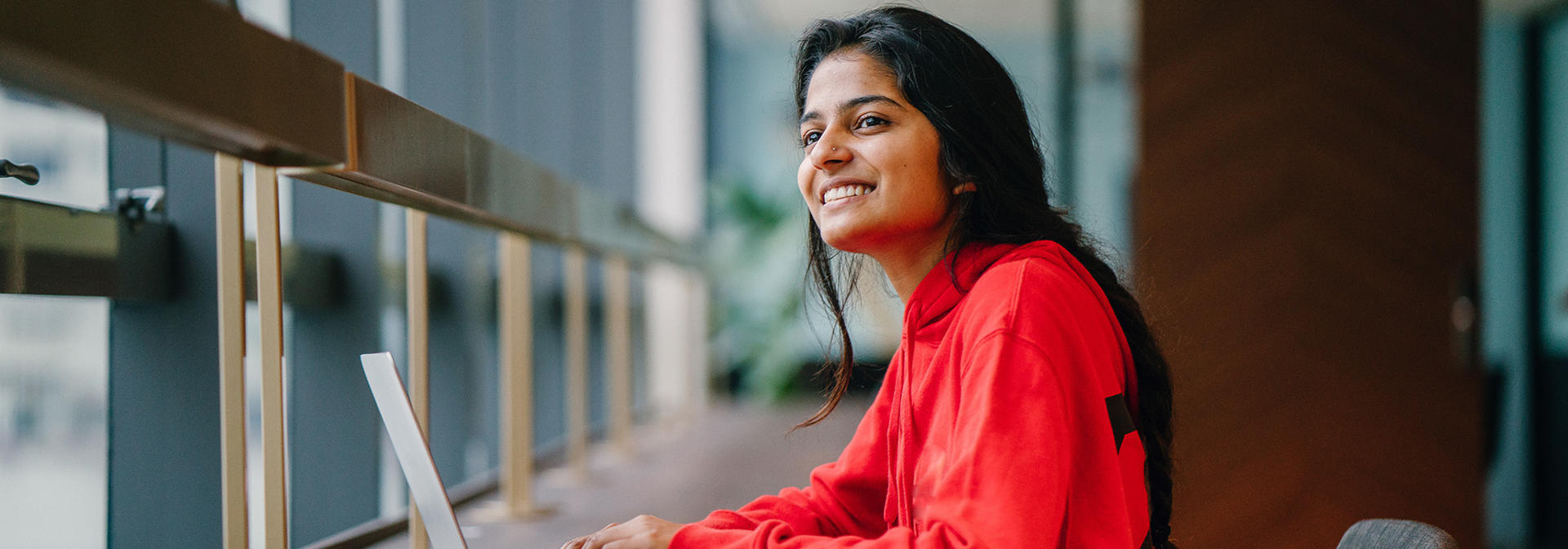 A student looks out of the window while working at her laptop.