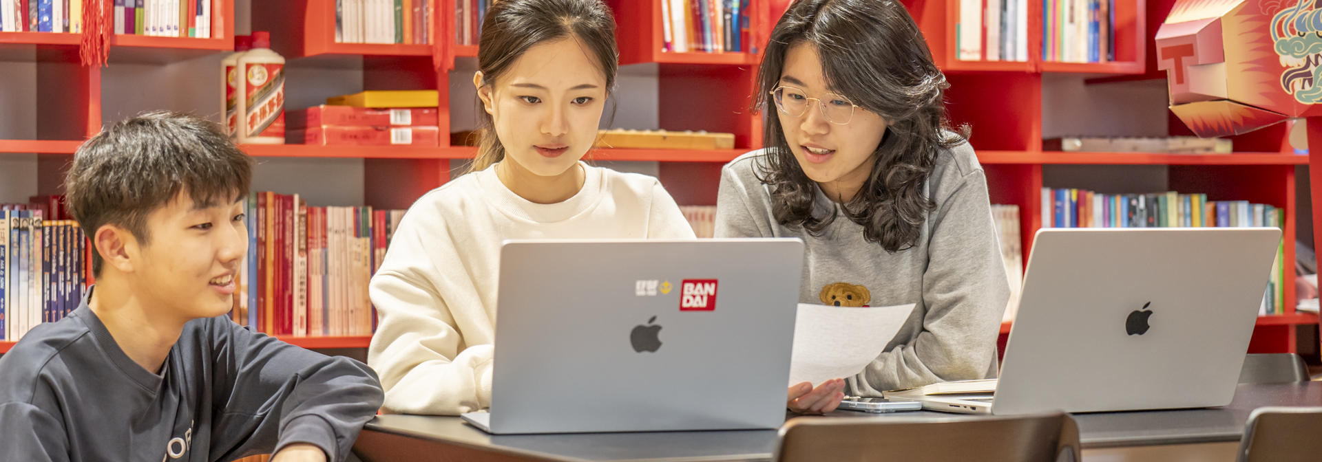 International students sit at a table with shelves of Chinese books and decorations behind them