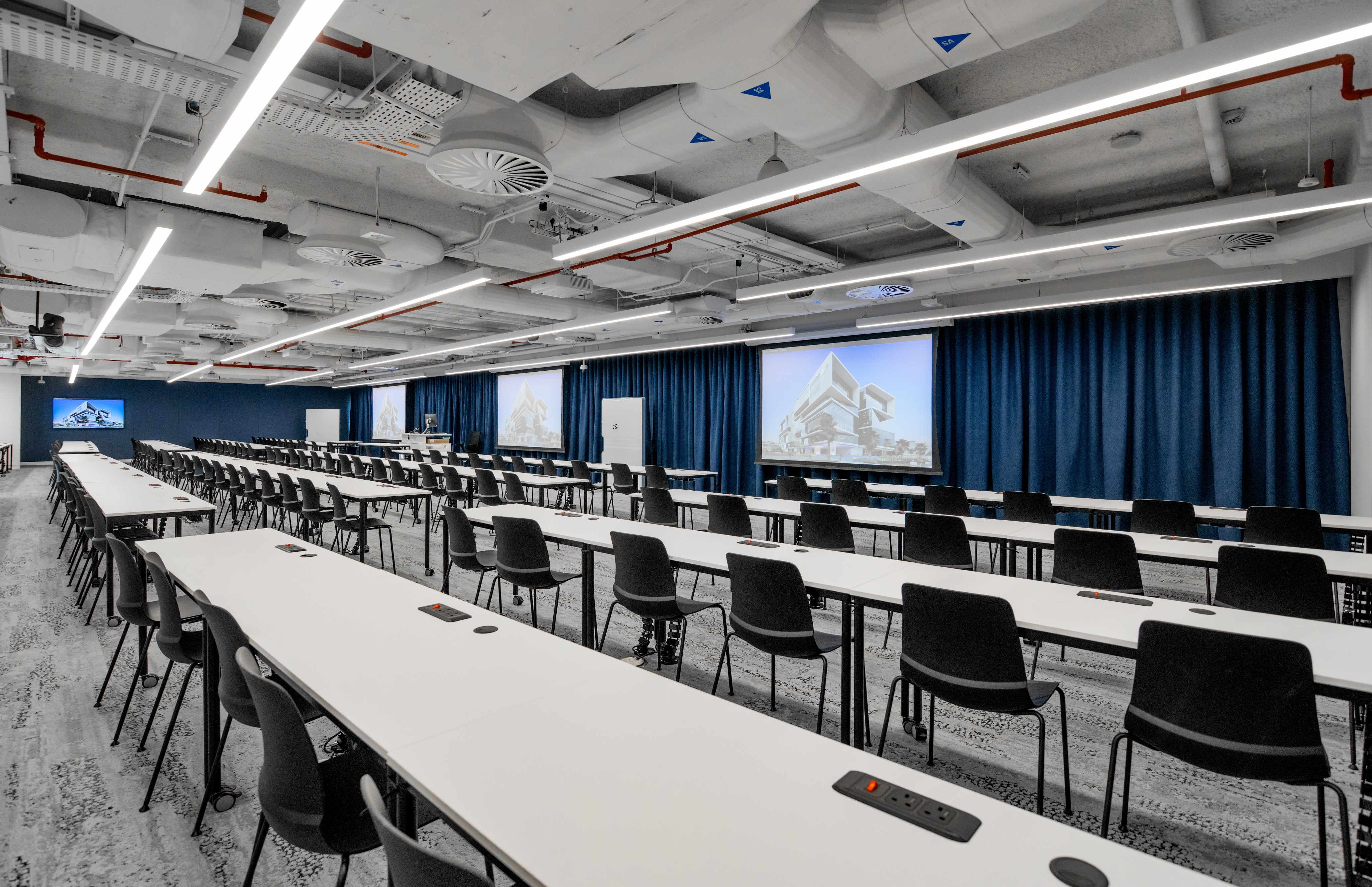 rows of continuous desk with black chairs facing blue curtains