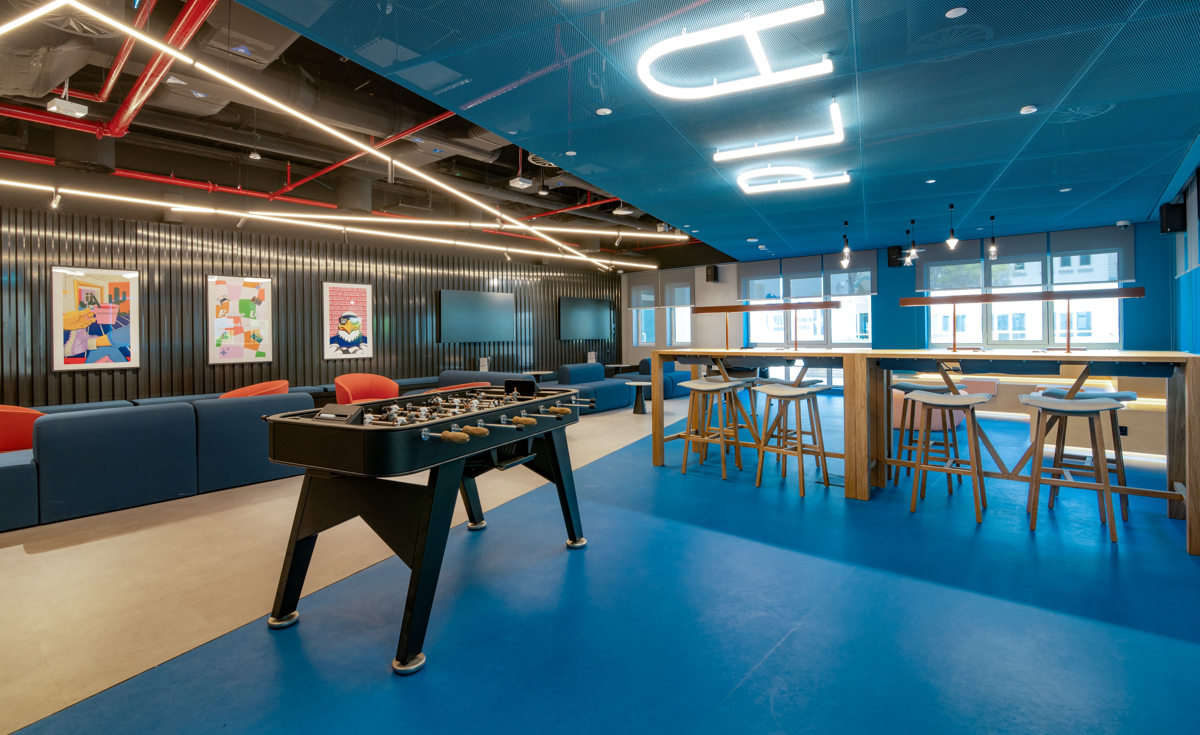 a lounge space with blue floor, walls and ceilings. Featuring a foosball table and tall seats and desk