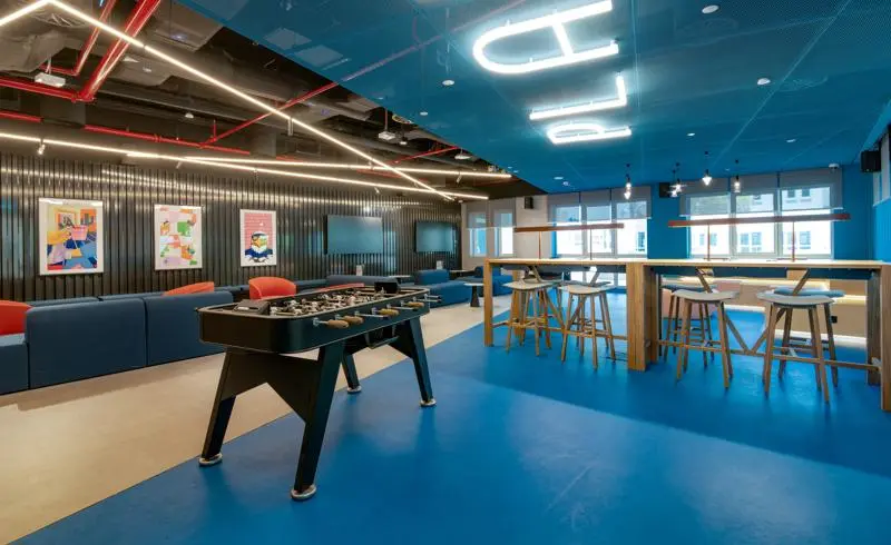 a lounge space with blue floor, walls and ceilings. Featuring a foosball table and tall seats and desk