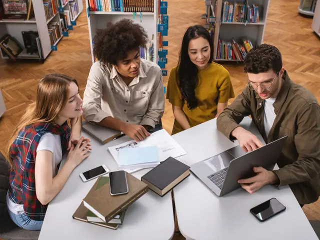 Three individuals working on a computer in a library