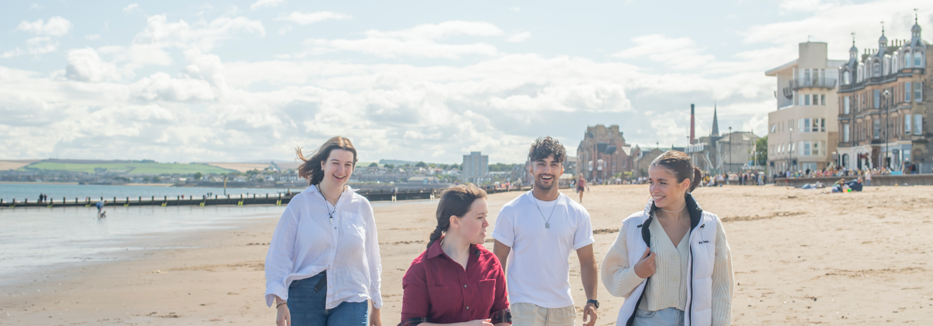Four individuals walking across a beach with a town in the background.