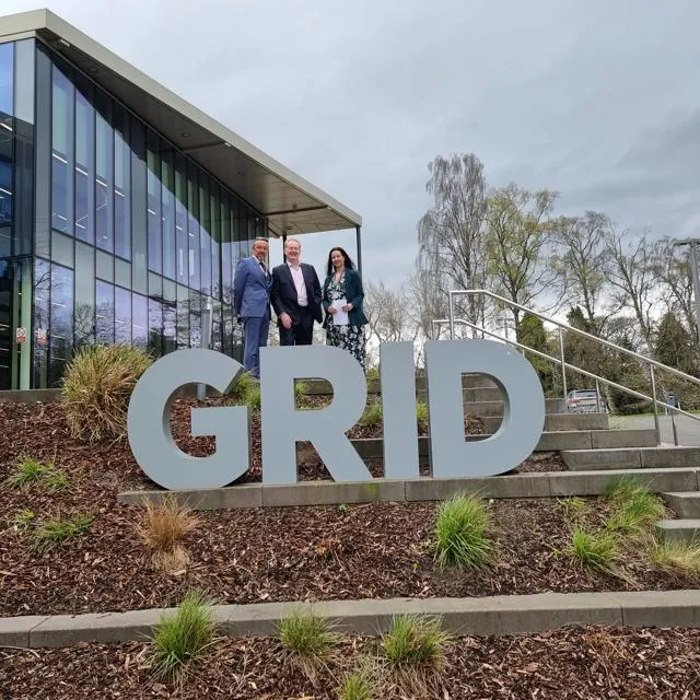 Three people stand behind the Heriot-Watt University Global Research Innovation and Discovery (GRID) sign in Edinburgh
