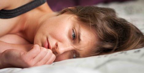 Image shows a woman lying on bed, appearing upset.