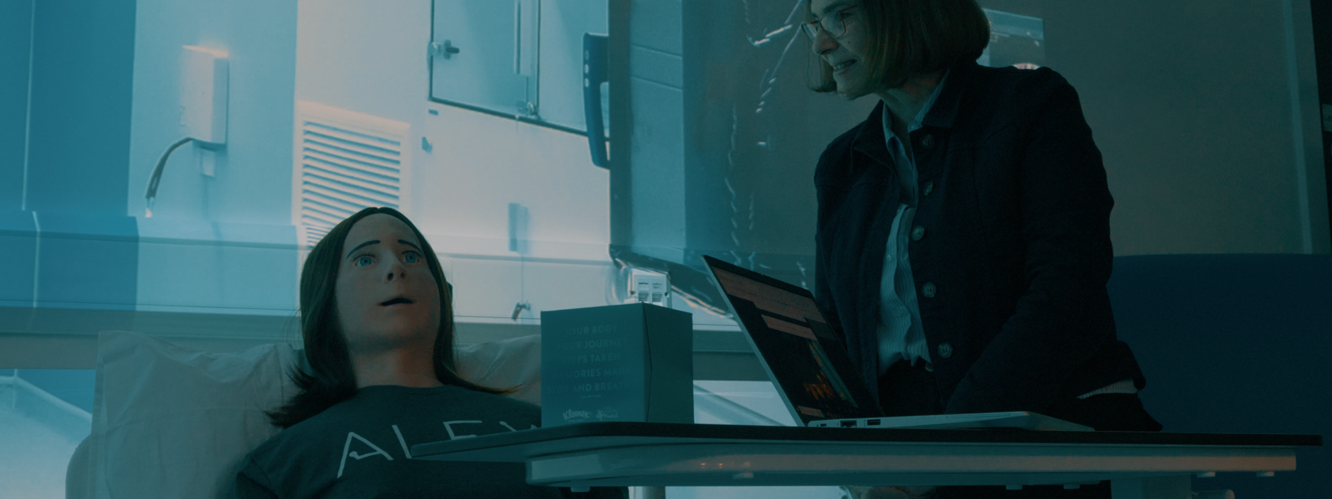 Alex robot in simulated hospital environment with staff performing tests.