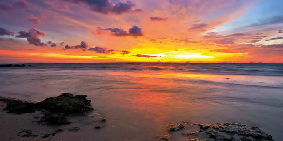 A vibrant sunset paints the sky in hues of orange, pink, and purple above a calm North Sea.