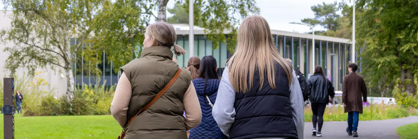 Individuals walking towards a building with trees and nature either side.
