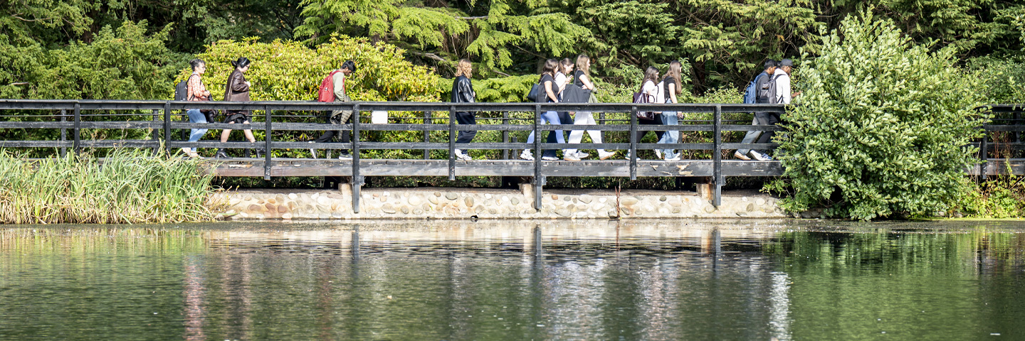 group of students cross the bridge over the Loch, with a clear sky and lush green surroundings.