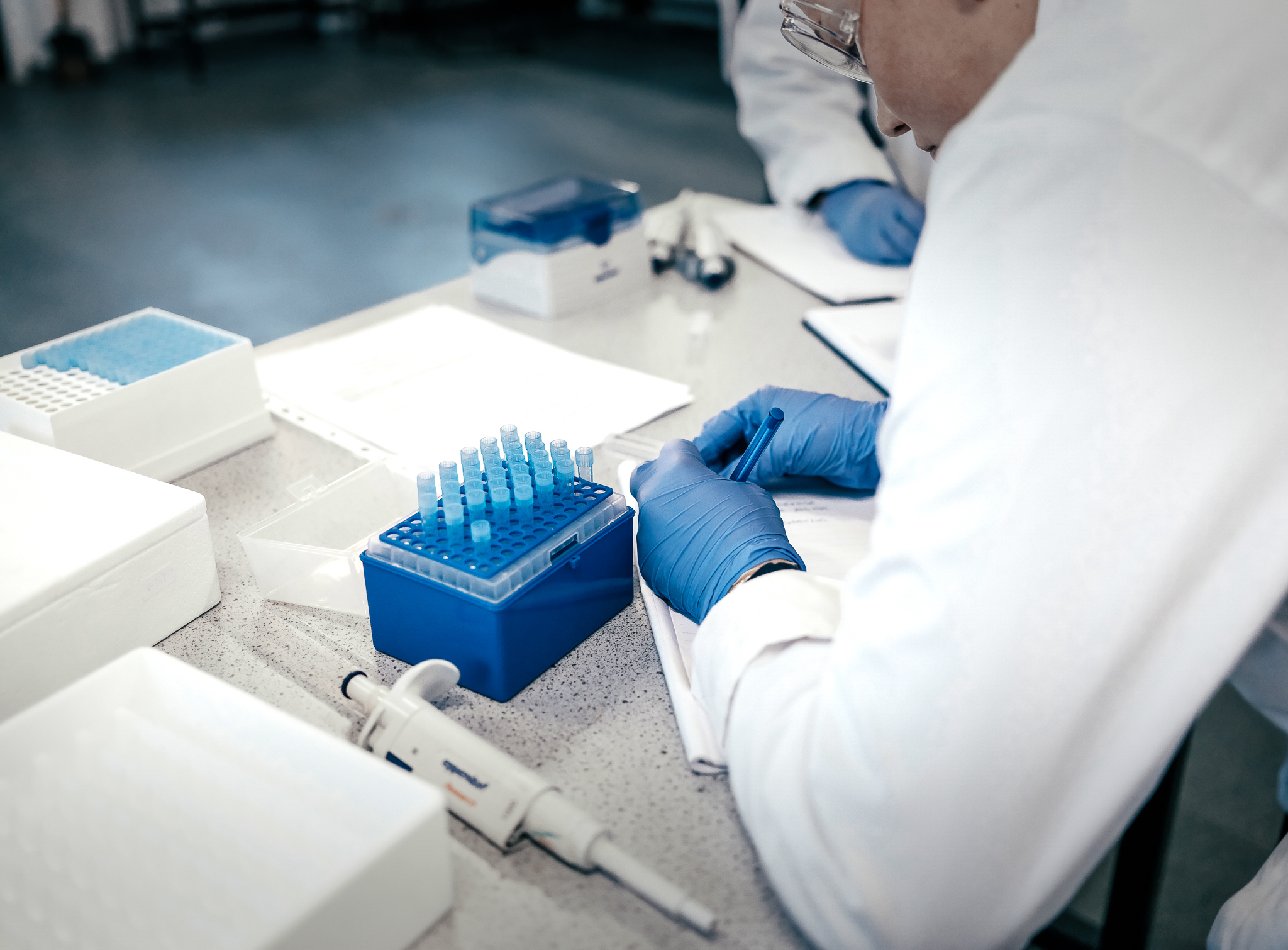 Students in a laboratory document sample details in a notebook.