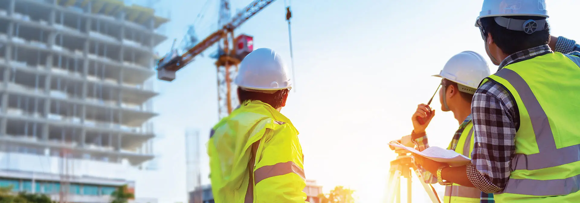 Three construction workers standing together on a construction site, wearing hard hats and safety vests.