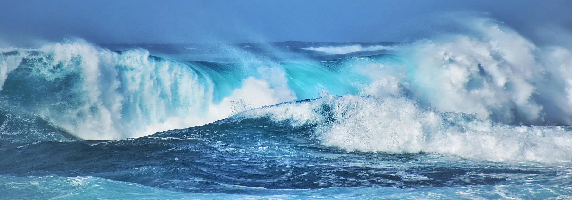 Waves surge and crash in the ocean, framed by a vibrant blue sky, highlighting the force of nature.