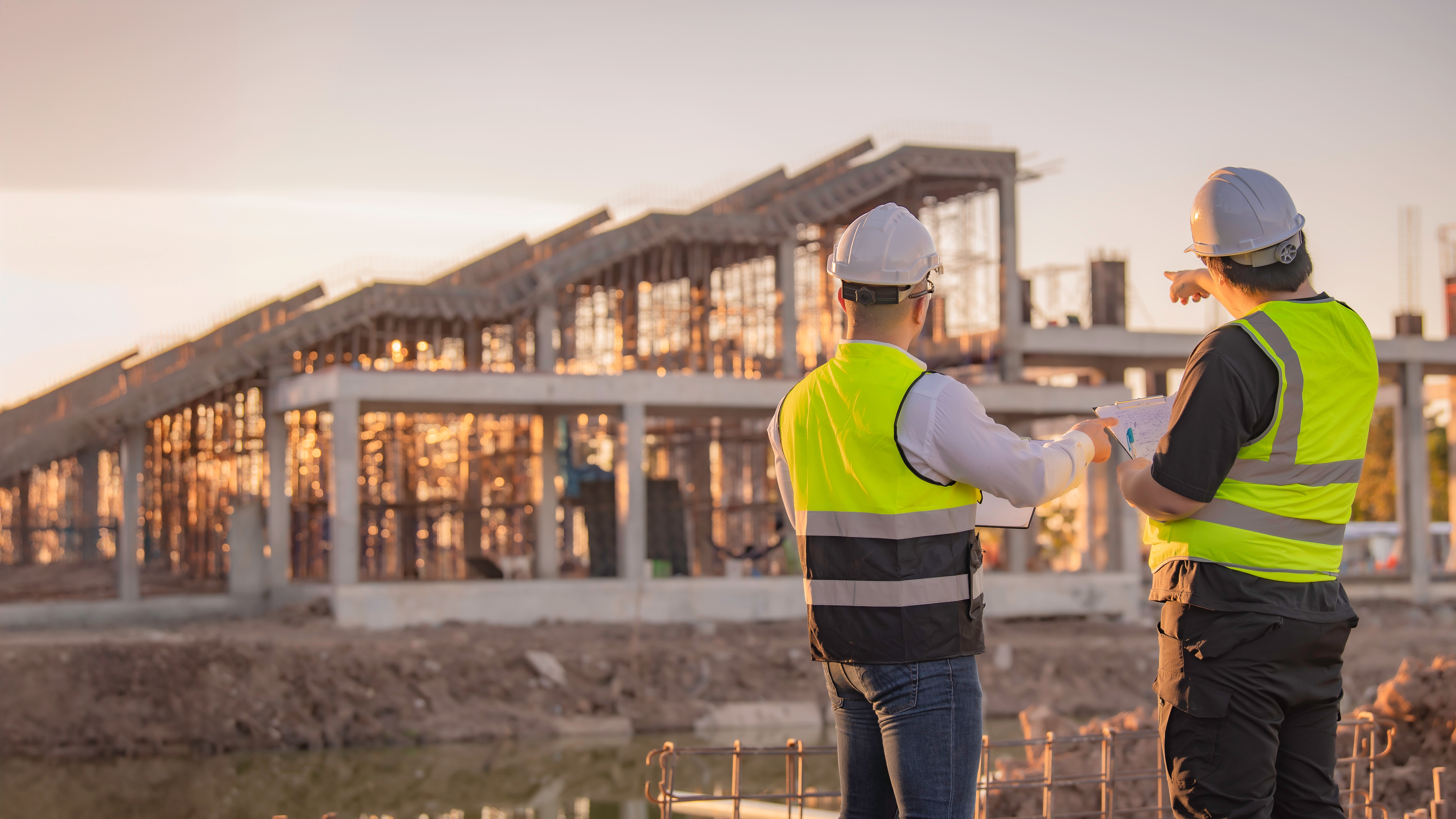 Tow engineers in high visibility vest and white hard hats inspecting construction site from far