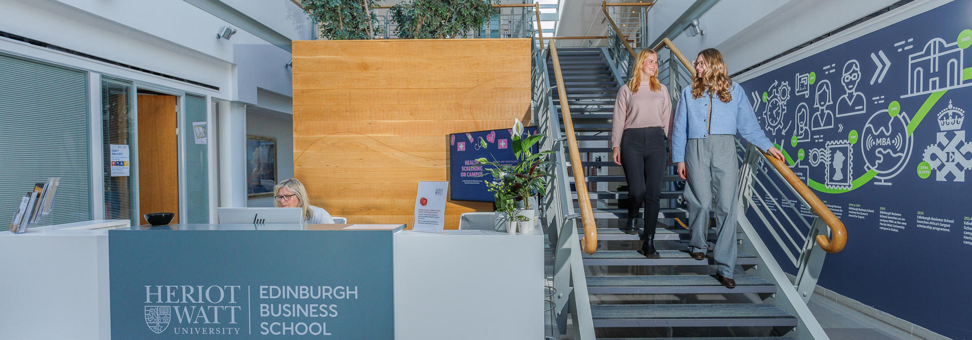 Two students in the Edinburgh Business School walking down the stairs beside reception.