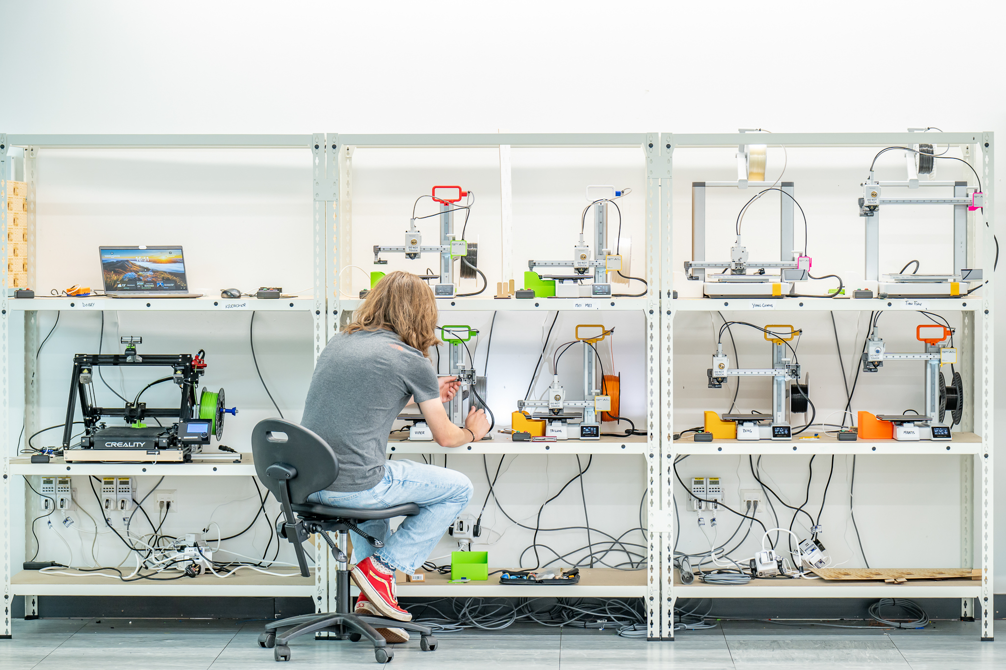 A wall of 3d printers, a student working on one of them 