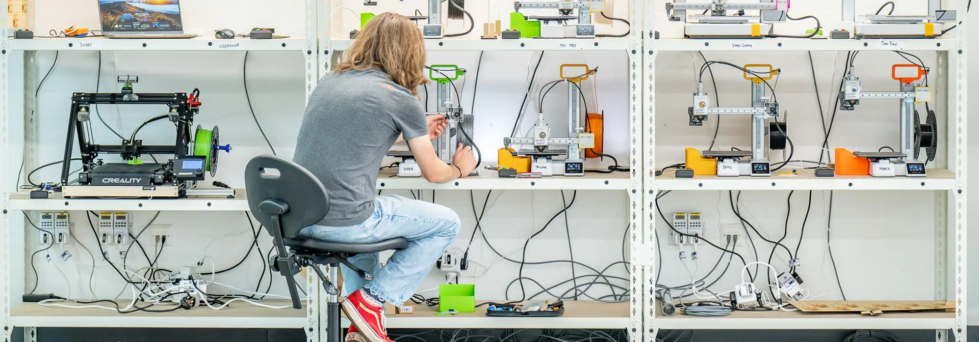 A wall of 3d printers, a student working on one of them