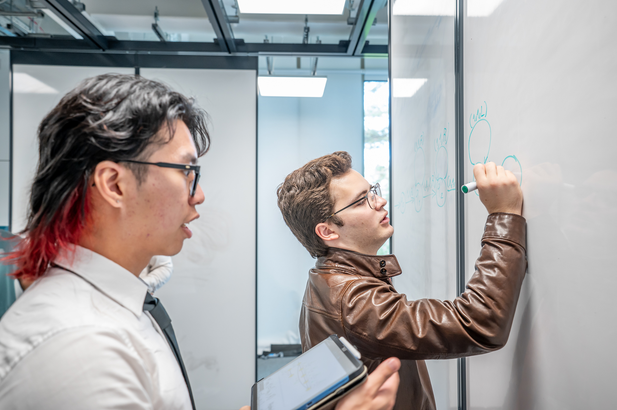 Students writing on a whiteboard and working on a question