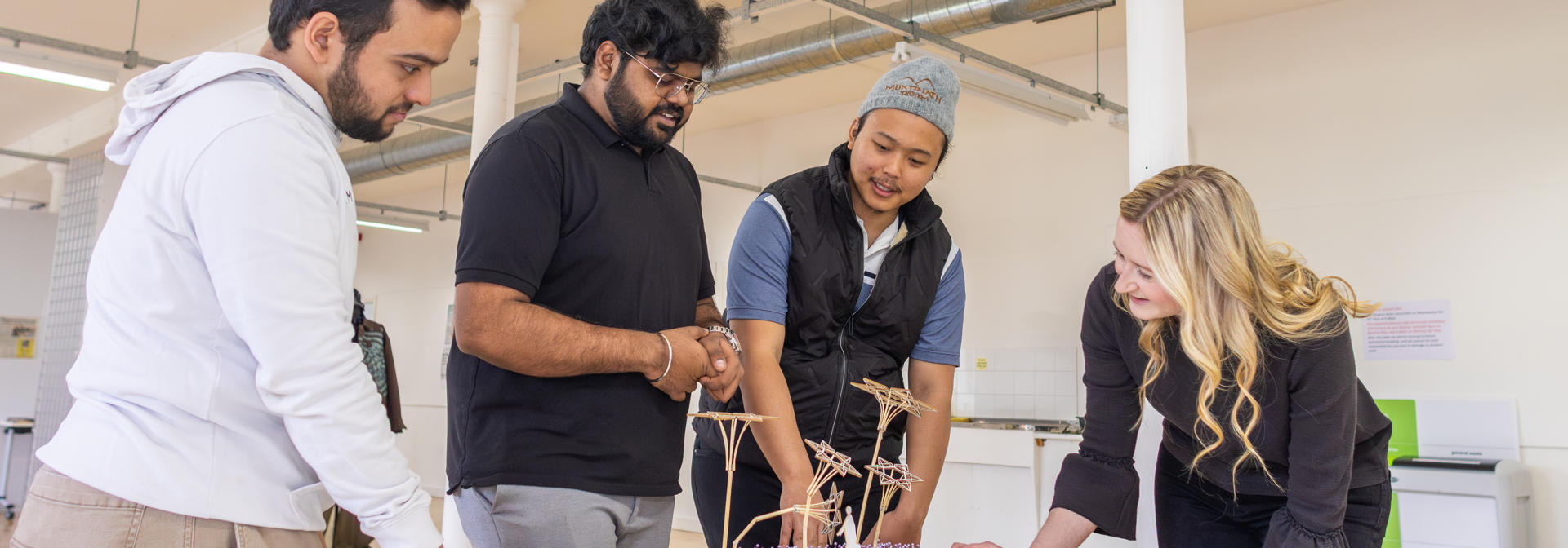 Postgraduate students discuss an intricate model design with an academic in the workspace.