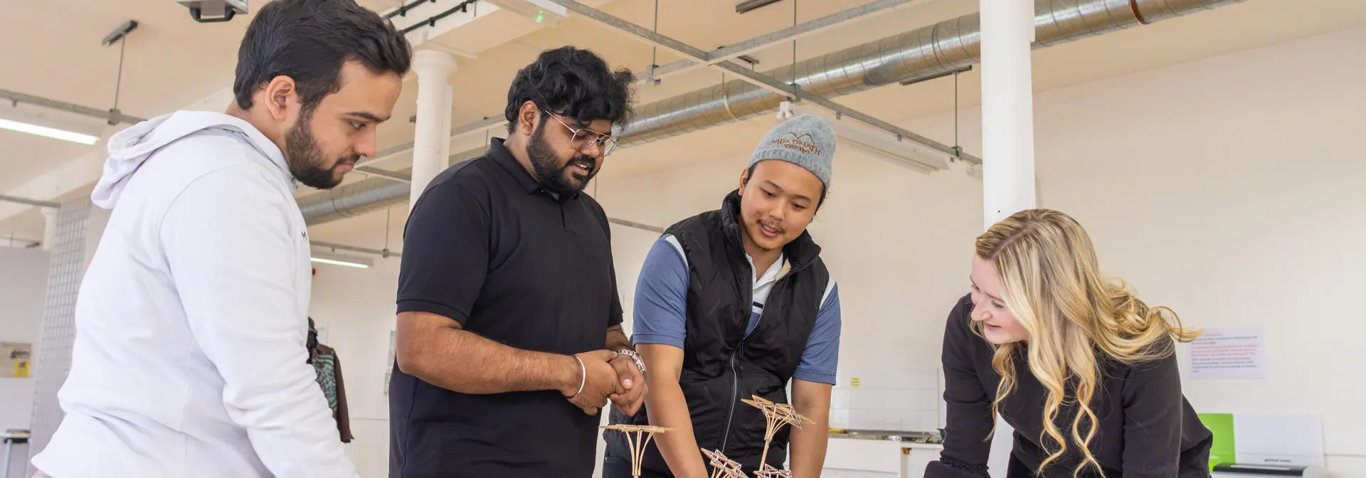Postgraduate students discuss an intricate model design with an academic in the workspace.