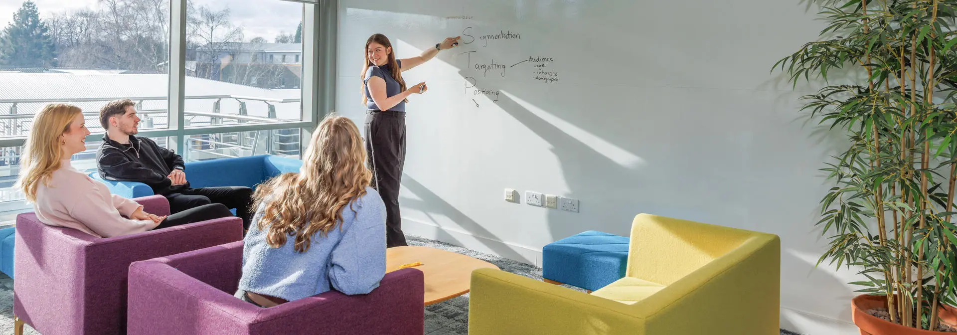 One student presenting at a whiteboard, to three students listening