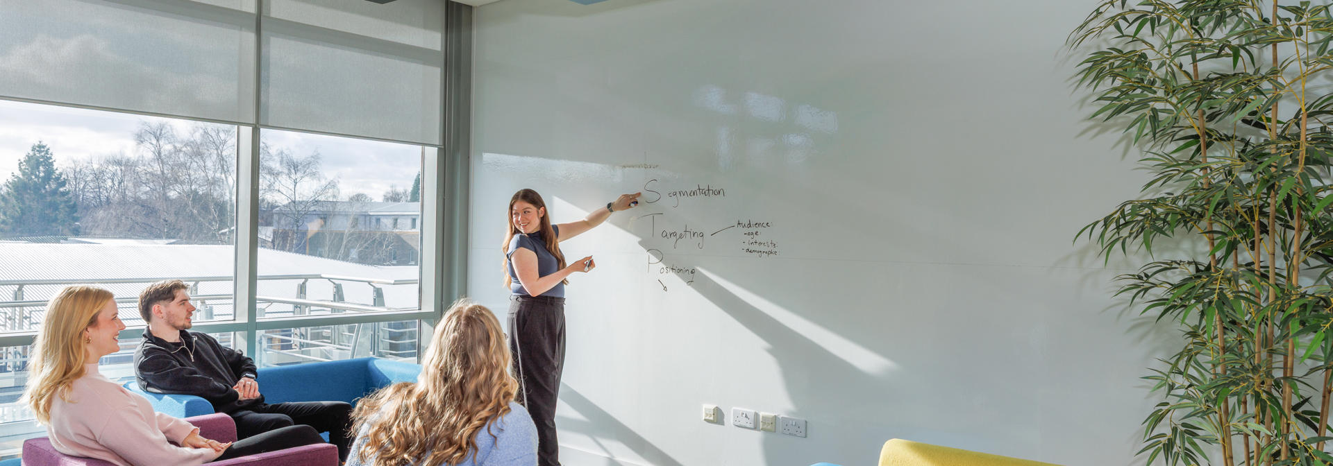 One student presenting at a whiteboard, to three students listening