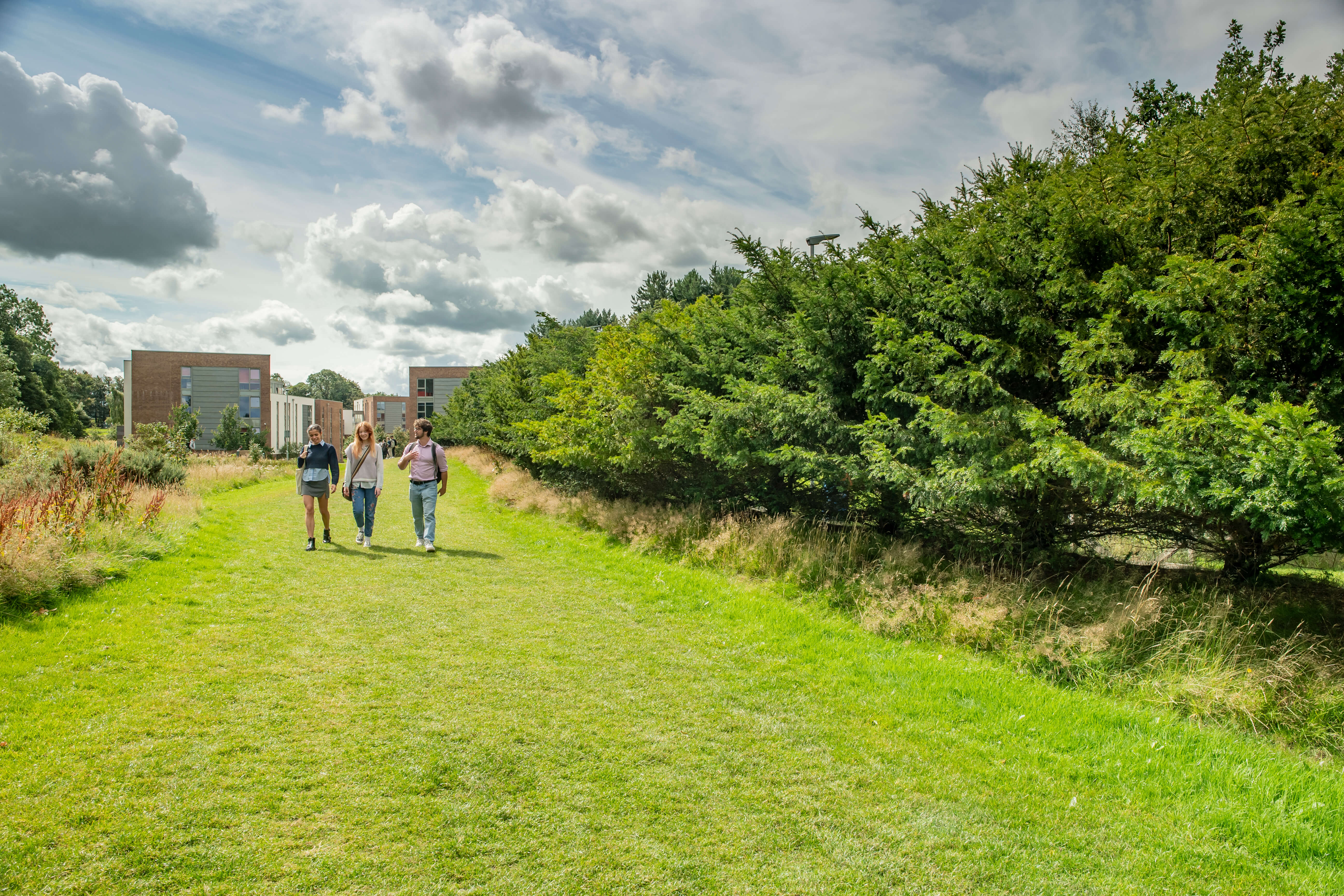 Three students walking on the grass path from the student halls, Edinburgh Campus.