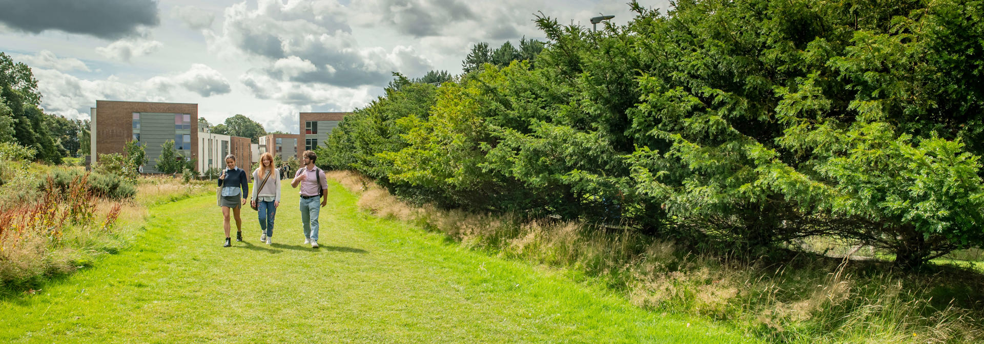 Three students walking on the grass path from the student halls, Edinburgh Campus.