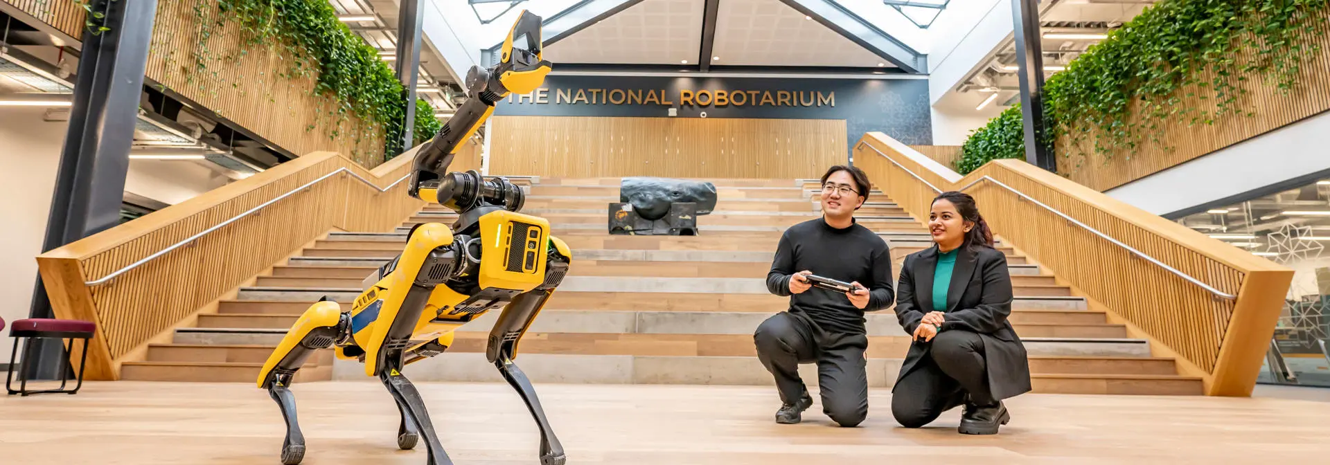 Two students operate a robot dog using a handheld console at the National Robotarium