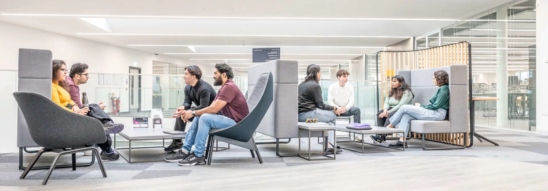 Two groups of students sitting in booths talking in a modern building