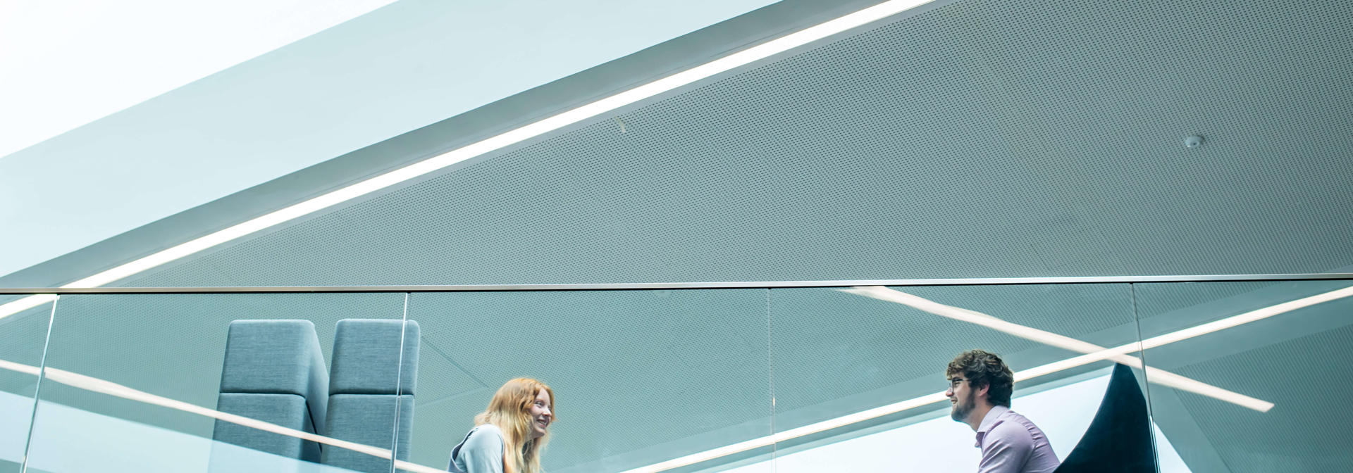 View from below of two students sat having a conversation on a higher floor of a modern building