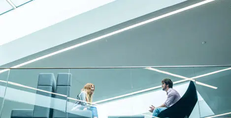 Two students seated opposite one another on the mezzanine floor of the GRID building viewed from the ground floor
