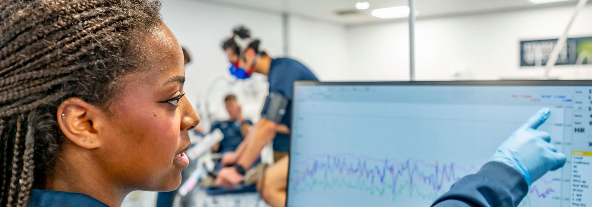 A Sport and Exercise Science student monitors a cyclist's performance data on a computer monitor