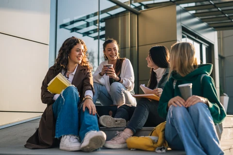 Four students sitting outside together drinking coffee.
