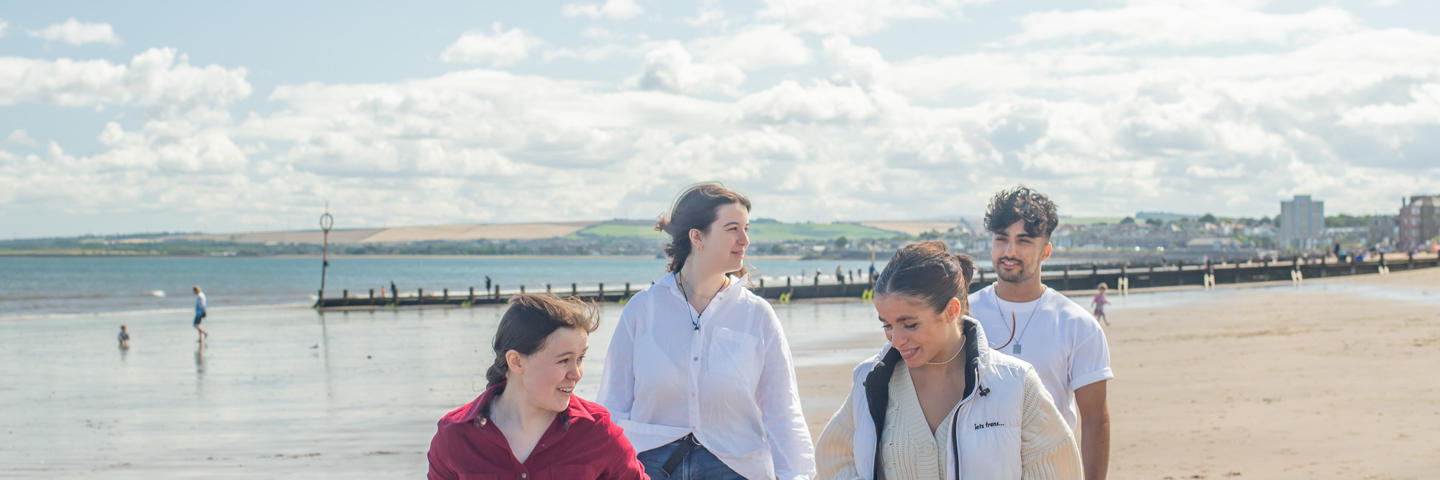 Four individuals walking on a beach on a sunny day.